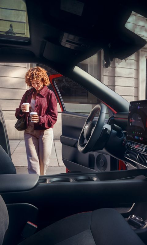 A woman holding cups in both hands walking into Hyundai IONIQ 3.