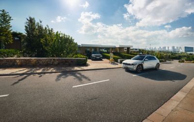 A woman and a Spot robot approaching an IONIQ 5 robotaxi outside a suburban house.