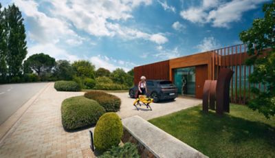 A person walking around the back of an all-electric Hyundai IONIQ 5 next to a house.