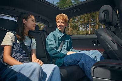Two smiling young people in a IONIQ 5's back seat, with pine trees visible through the windows and a sunroof overhead.