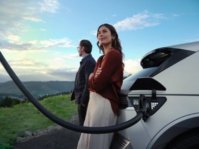 A woman and a man leaning on the tailgate of Hyundai IONIQ 5 as it is plugged in to charge.