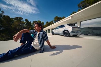 A man sitting in a relaxed pose near the Hyundai IONIQ 5 EV vehicle on a bright, sunny day.