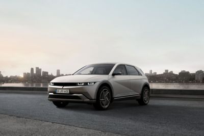 Three-quarter view of new Hyundai IONIQ 5 parked by a river with a city skyline in the background.