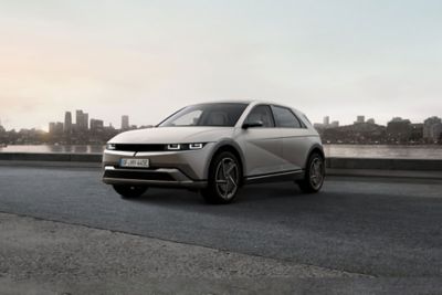 Three-quarter view of new Hyundai IONIQ 5 parked by a river with a city skyline in the background.