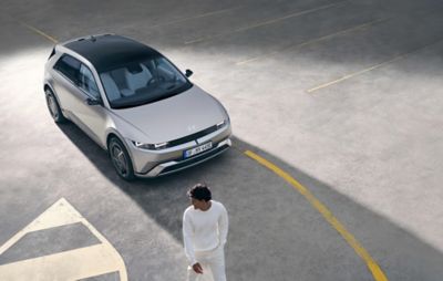 Three quarter view of the new Hyundai IONIQ 5 seen from above, parked, and a man walking away.  