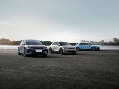 Three Hyundai IONIQ 5 cars in different colours parked with a city skyline in the background.