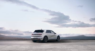 Driekwart achteraanzicht van de nieuwe Hyundai IONIQ 5 met een bewolkte lucht op de achtergrond.