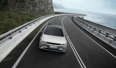 Vista frontale di Hyundai IONIQ 5 in grigio mentre percorre una strada costiera piena di curve