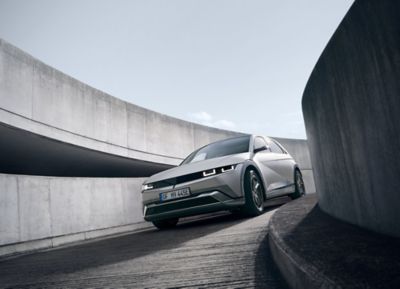 Three-quarter view of the new Hyundai IONIQ 5 in grey driving down a curving concrete ramp.