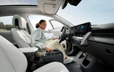  A woman sitting in the driver’s seat of the IONIQ 5, taking a mobile phone from the centre console.
