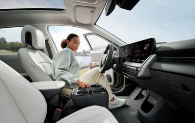 Vrouw achter stuur nieuwe Hyundai IONIQ pakt smartphone uit oplaadpad in middenconsole.