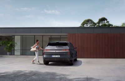 Vrouw opent bestuurdersportier van geparkeerde nieuwe Hyundai IONIQ 5 N Line met woonhuis op achtergrond.