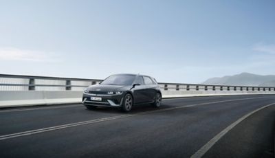 Front three-quarters view of the new Hyundai i30 Hatchback in grey, parked outside a modern house.