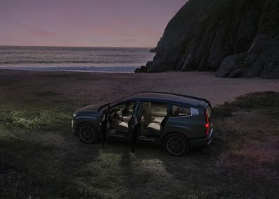 La IONIQ 9 garée au bord de la mer la nuit, portes ouvertes et éclairage intérieur allumé.