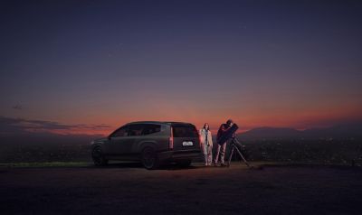 Et ungt par bruker IONIQ 9 til å lade en stjernekikkert i et vakkert naturlandskap. Foto.