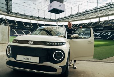 Mario Götze steht im Deutsche Bank Park Stadion vor der Heckklappe eines Hyundai INSTER. 