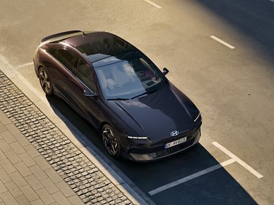 HYUNDAI IONIQ 6 viewed from above driving along a sunlit road, highlighting its streamlined shape and clean lines.