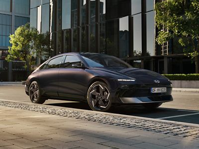 HYUNDAI IONIQ 6 parked on a quiet urban street in front of modern glass buildings, showcasing its elegant side profile and distinctive styling.
