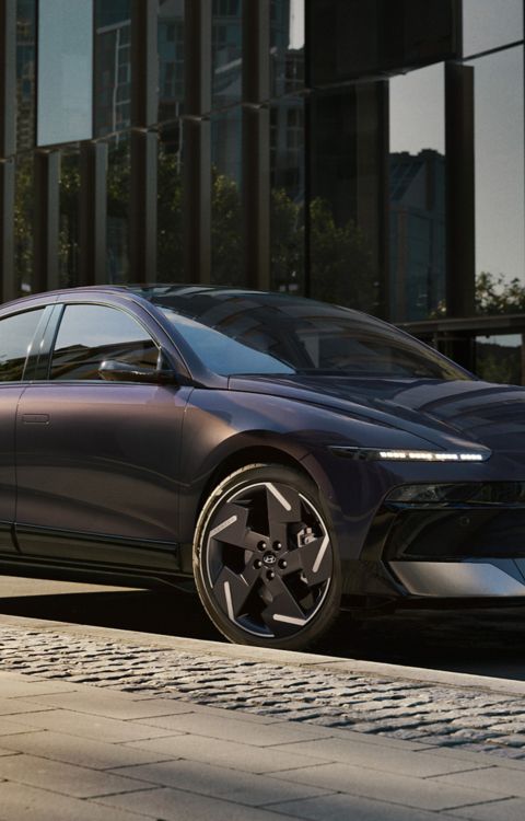 HYUNDAI IONIQ 6 parked on a quiet urban street in front of modern glass buildings, showcasing its elegant side profile and distinctive styling.