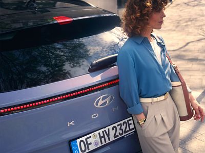 Rear view of Hyundai KONA Electric with a person leaning against the tailgate.
