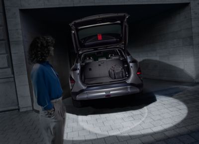 A woman in a dark garage next to the KONA with LED trunk and tailgate lights lighting the scene.