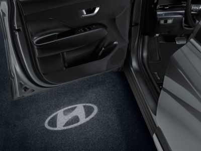 Hyundai logo projected on garage floor by LED door projectors from the open door of the KONA.