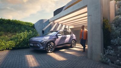 The Hyundai KONA Electric bathed in sunlight with a man walking away from a garage.