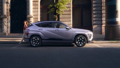 A woman walking behind Hyundai KONA parked on the city street.