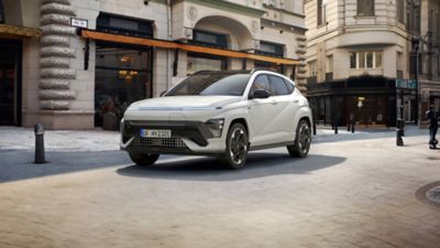 Hyundai KONA Electric N Line bielej farby Serenity White Pearl s čiernou strechou pred hotelom.