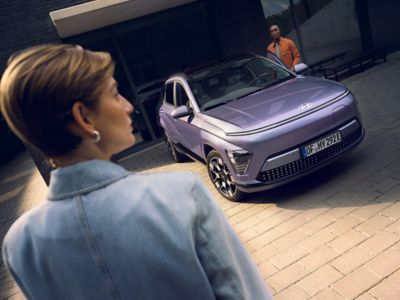 En dame står og ser på en parkert KONA Electric. Foto.