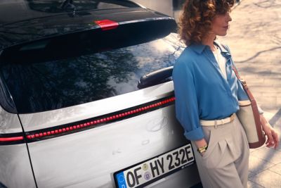 Vrouw leunt tegen achterzijde Hyundai KONA.
