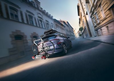 Hyundai KONA Electric driving down a city street with a bike on a bike carrier for tow bars.