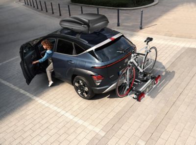 A woman exiting the Hyundai KONA with a bicycle, which is fixed to a bike carrier for tow bars.