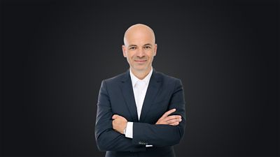 Manfred Harrer, Head of Genesis and Performance Development Tech Unit, standing with arms crossed against a dark background.