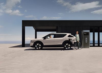 A man leaning on  the Hyundai NEXO as it is charging hydrogen at a station.