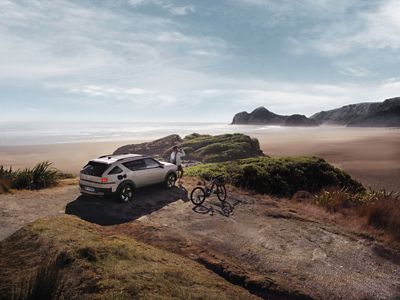 Hyundai NEXO with an e-bike plugged into it charging via V2L while parked by cliffs near the beach.	