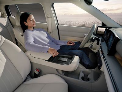 A woman sitting in the front seat of the Hyundai NEXO at sunset with the ocean in background.	