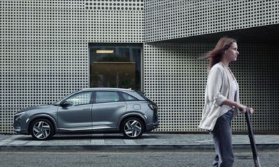 Donna che guida un monopattino elettrico con Hyundai NEXO sullo sfondo 