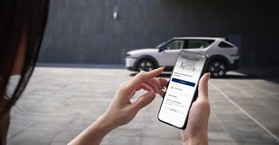 Hyundai NEXO in the background. A person is checking the myHyundai app.