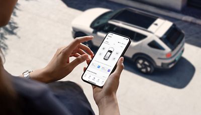Woman looking at her smartphone with myHyundai app. In background is Hyundai NEXO parked on the street.