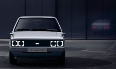 Vooraanzicht Hyundai PONY EV Heritage tegen donkere achtergrond.