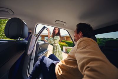 A woman in a green dress holds the door open for a man in the back seat of an IONIQ 5 robotaxi.