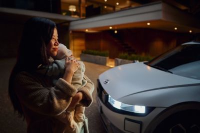 A woman holding a baby newxt to the IONIQ 5.