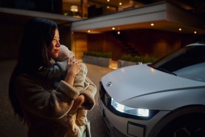 A woman holding a baby next to the IONIQ 5.