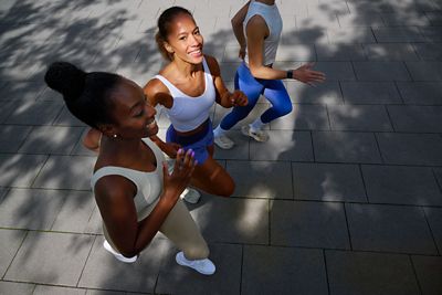 Spor kıyafetleri giymiş üç koşucunun güneşli bir kaldırımda koşarken yukarıdan görünümü. 