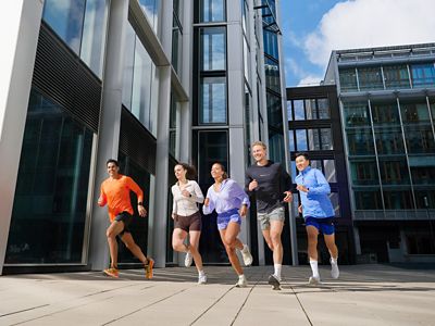 Modern bir ofis binası önünde jogging yapan altı koşucu. 