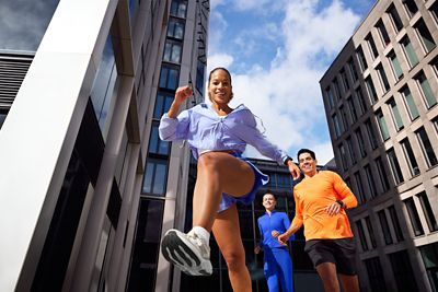 Low-angle shot of a runner leaping past the camera with others following in a city plaza.
