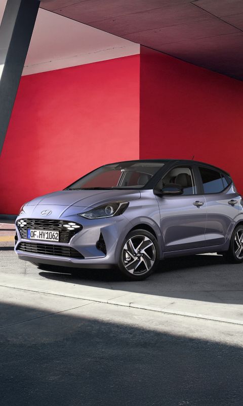 Hyundai i10 hatchback front three-quarter parked under a modern overhang with bold red and blue walls.