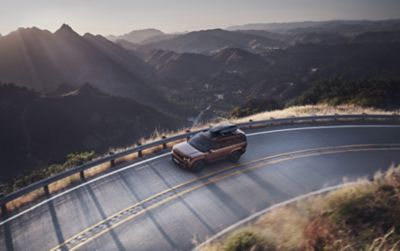 The Hyundai SANTA FE seen from above, with a roofbox, driving round a curve of a mountain road.