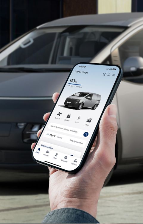 myHyundai app displayed on a smartphone in front of a Hyundai Staria Cargo vehicle.